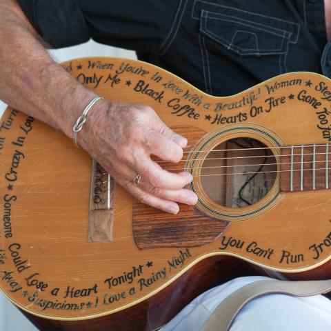 A person strums a guitar covered in hit song names. 