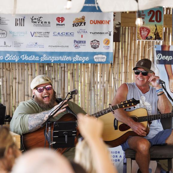 two artists sitting on stage smiling and performing