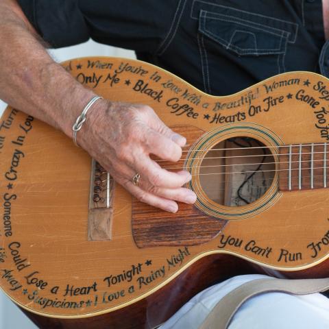 A person strums a guitar covered in hit song names.